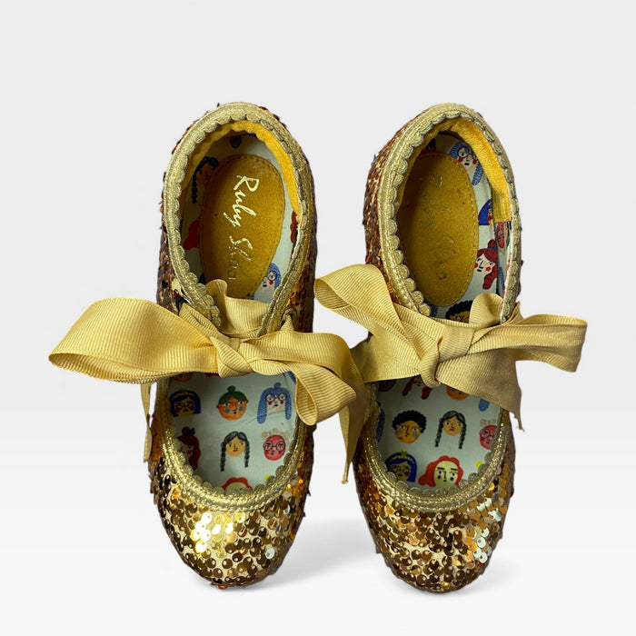 Gold sequin shoes with yellow ribbons on a white background
