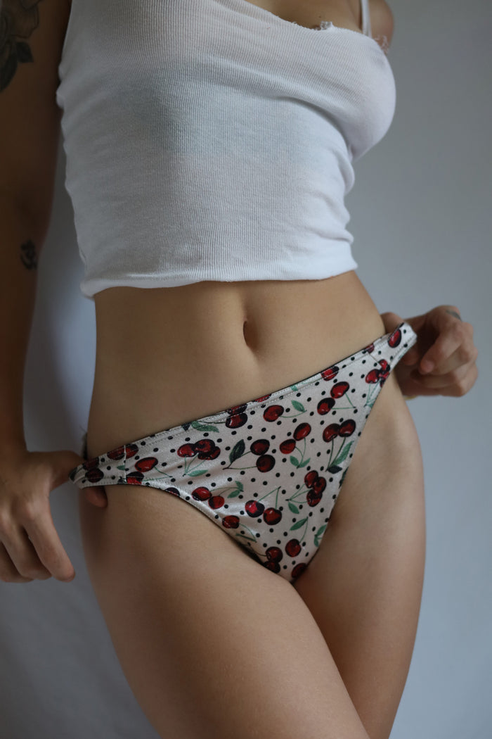 Cherry-print satin thong panties on model, side view showing full waistband