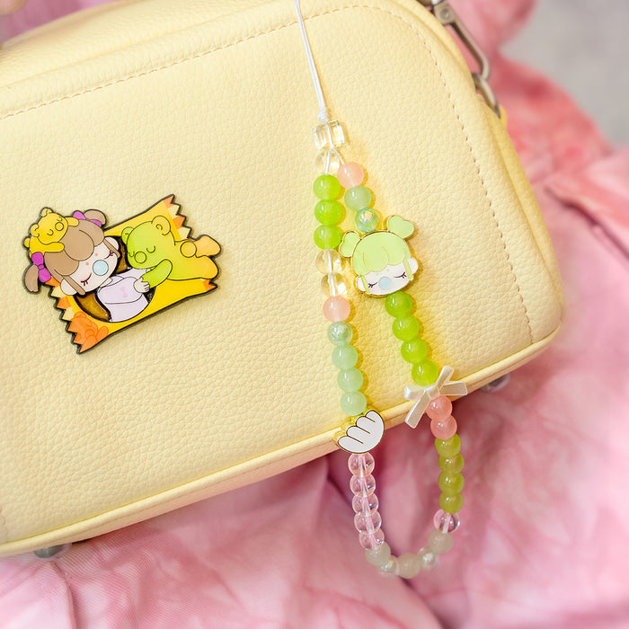 Rolife Nanci Sweet Time Cupid lanyard in green beads attached to a yellow handbag beside a matching enamel Nanci candy-wrapper badge pin.