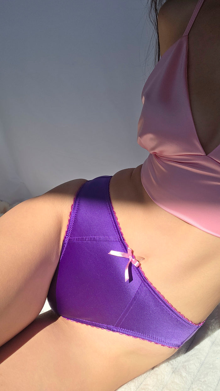 Violet satin thong-style panties with lace trim and center bow, side view