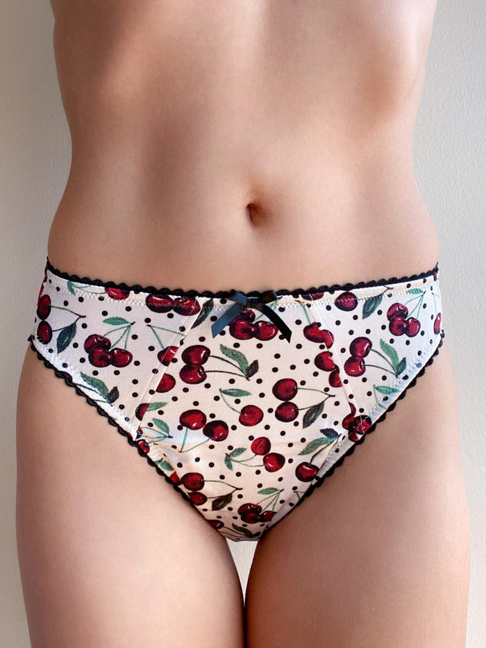 Cherry print bikini-brief panties with dark lace trim on body, front close-up