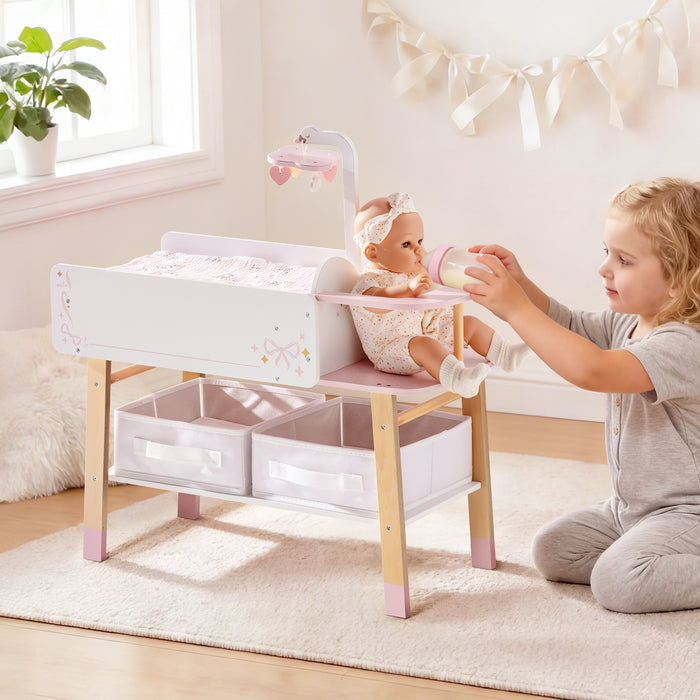 Toddler placing a baby doll in the ROBUD pink and natural wood changing table set up in a bright sunlit playroom.