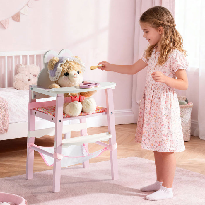 Girl in a floral dress feeds a stuffed bear seated in the ROBUD pink wooden doll high chair in a styled pastel nursery room.