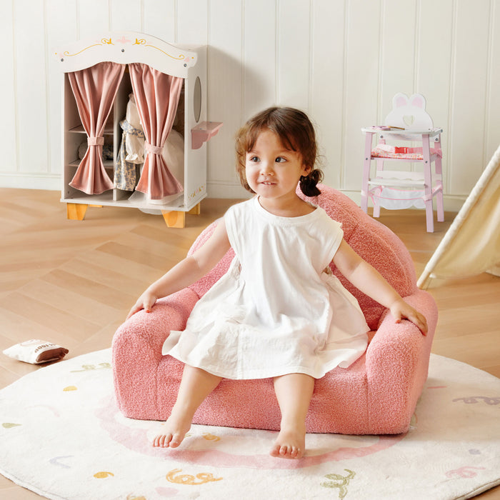 Girl in a white dress sits on the ROBUD pink teddy sofa with the princess doll wardrobe and high chair visible behind her.