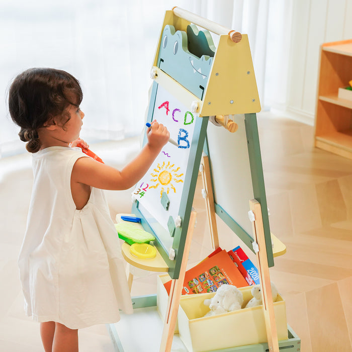 Toddler drawing letters on ROBUD Crocodile Easel in a sunny room with plants and toy guitar in background