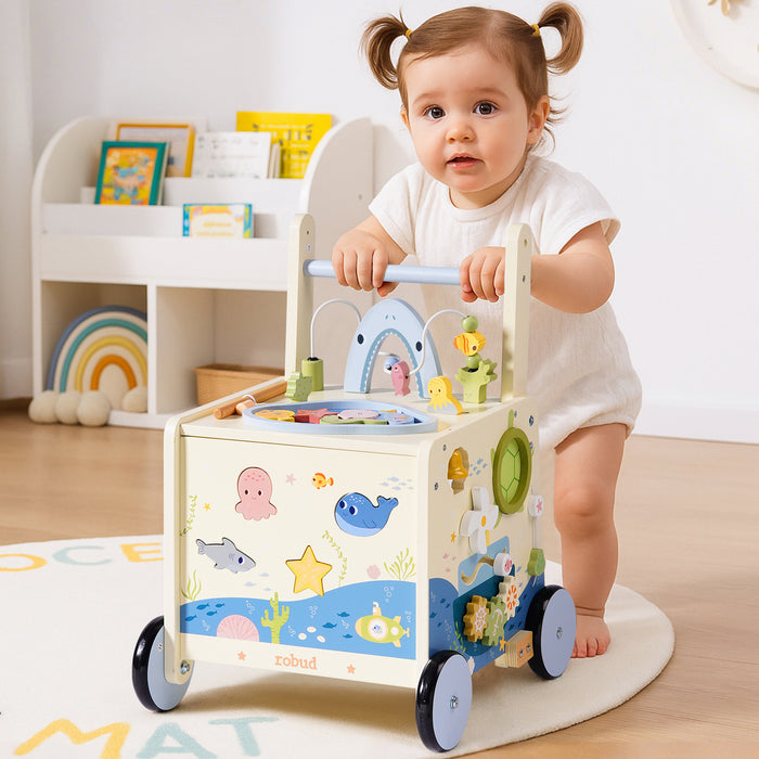 ROBUD Wooden Baby Push Walker Underwater World with toddler girl pushing the blue and white ocean-themed walker in bright playroom setting