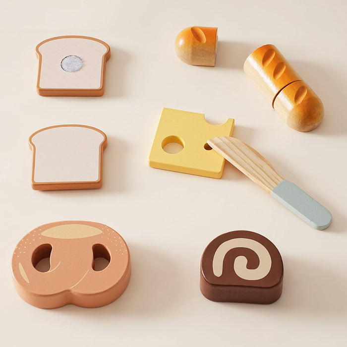 ROBUD wooden bread and dessert cutting playset pieces flat lay on cream background showing toast halves, yellow cheese, baguette halves, pretzel, swiss roll, and wooden knife