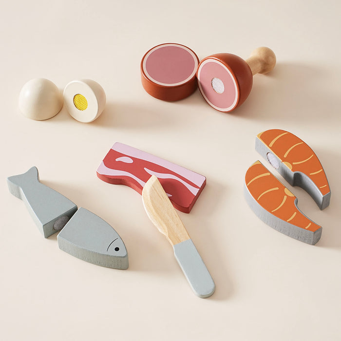 ROBUD wooden meat cutting playset flat lay on cream background showing egg and chicken leg halves, salmon steak, red bacon strip, grey fish, and wooden knife