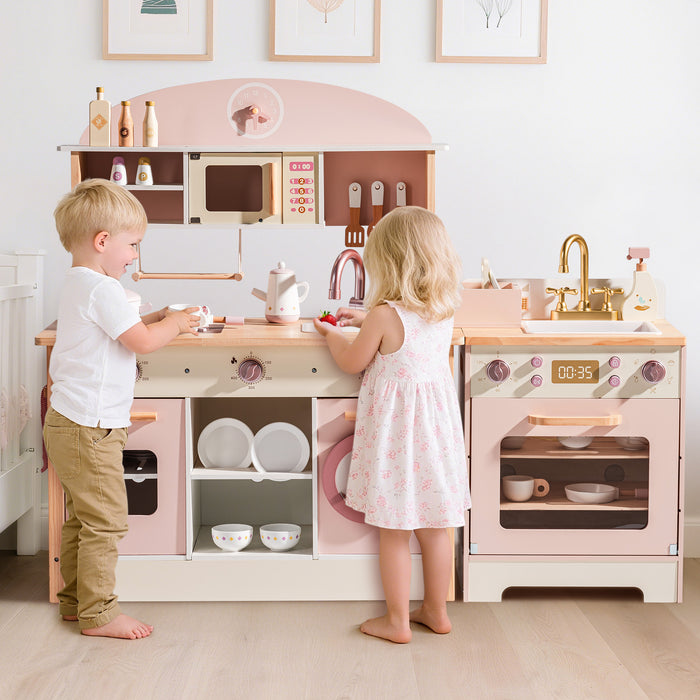 Two children standing at the ROBUD Pink Wooden Kitchen PlaySet in lifestyle room setting with bunting overhead