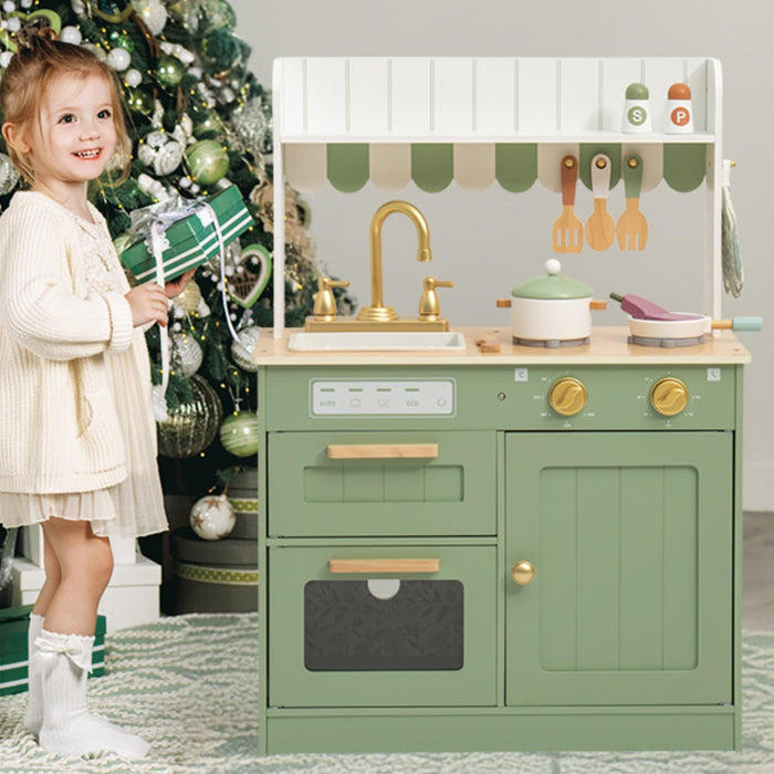 Young girl in cream dress playing beside ROBUD Olivia green wooden play kitchen set decorated near a Christmas tree