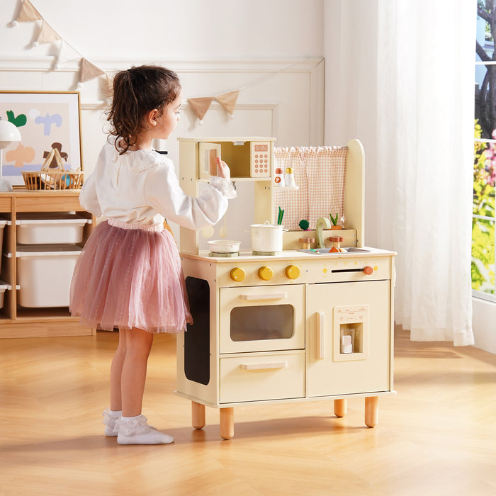 Girl in a pink tutu stands at the ROBUD cream wooden play kitchen, reaching toward the oven and refrigerator from the side.