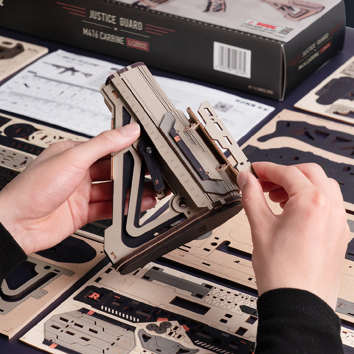 Hands assembling the wooden rifle model over its packaging box and cut wood parts sheet