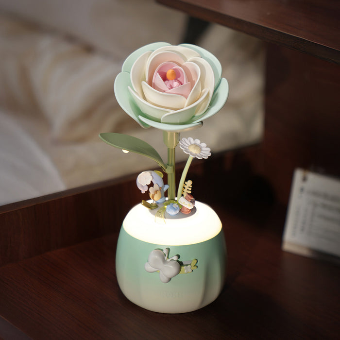 ROKR Minty Camellia Lamp AF02S glowing green rose night light with tiny fairy figurines placed on a dark wooden shelf beside books