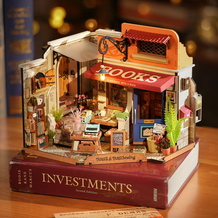 Rolife Corner Bookstore DIY miniature house with warm glowing interior displayed on a hardcover book cover, showing the red awning and tiny bookshelves