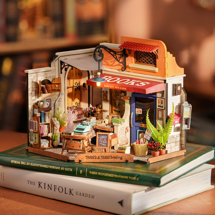 Rolife Corner Bookstore miniature house placed on a stack of books showing the full two-story wooden facade with Books signage and lit interior