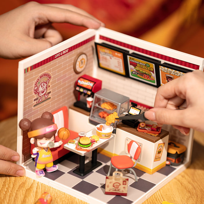 Rolife Yum Yum Burgers DW010 hands placing chicken piece into the miniature scene with character figure and food accessories inside the diner room