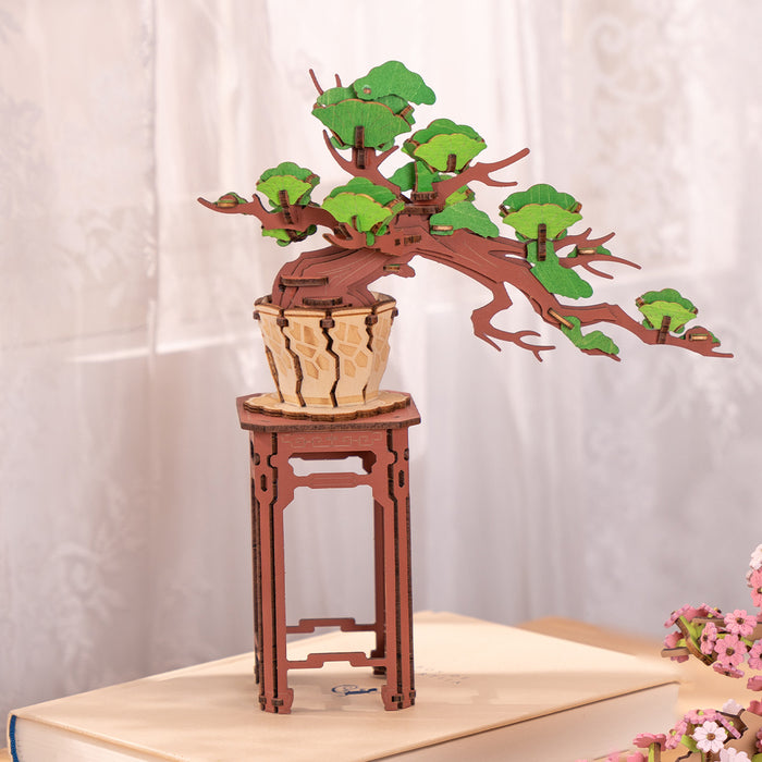 Rolife Evergreen Pine Bonsai TG510 with green foliage on wooden pedestal stand, soft pink backdrop