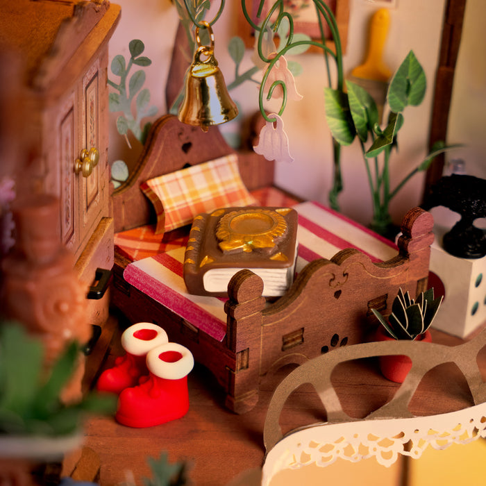 Hands assembling the Rolife Fairytale Tree House DG179 miniature fitting a decorative wooden drawer unit with miniature accessories and instruction guide on a light green surface