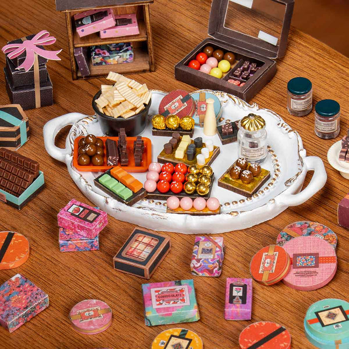 Rolife Henry's Chocolate miniature house DG174 top-down view showing an elaborate miniature chocolate shop tray filled with tiny chocolate shapes, gift boxes, colorful tins, and candy replicas.