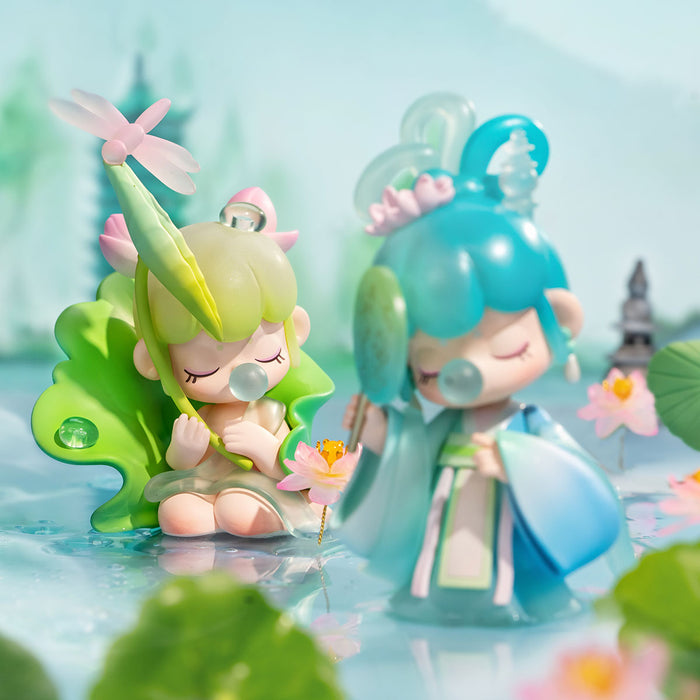 Two Rolife Nanci Poetic Beauty figures, a green leaf fairy and blue floral doll, posed beside a lotus pond scene