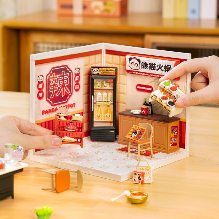 Hands opening the Rolife Panda Hot Pot DW020 Super Creator kit while a panda hotpot sign and illuminated drink fridge are visible inside the assembled room