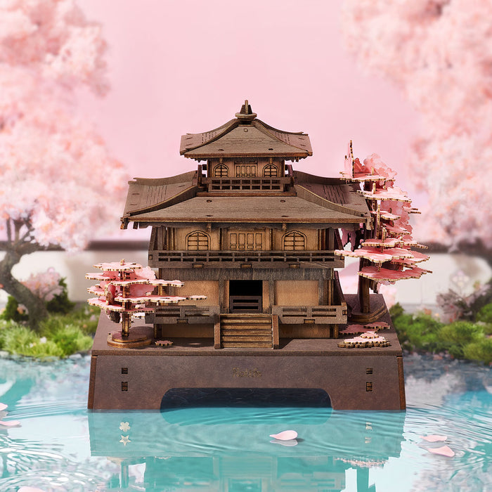 Rolife Sakura Pavilion TGA07 3D wooden puzzle hero shot showing the multi-tiered pagoda on a pink reflective base surrounded by cherry blossom petals