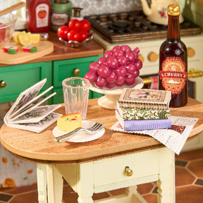 Rolife miniature kitchen detail with red grapes, a cherry beer bottle and stacked books on a cream round table