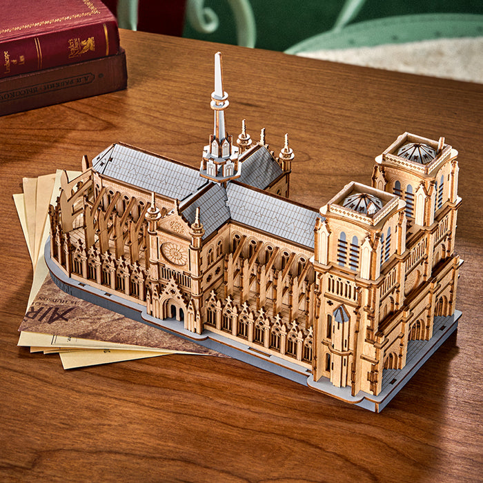 Rowood Paris Cathedral TG511 wooden puzzle front view showing the twin bell towers, arched portal, and intricate Gothic stonework details on a wooden desk by books