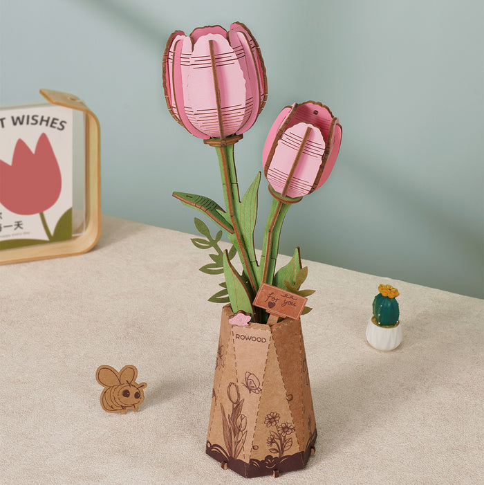 Rowood purple orchid wooden flower bouquet kit TW091 assembled with multiple blooms and green foliage displayed in a kraft paper vase on a desk beside a cactus
