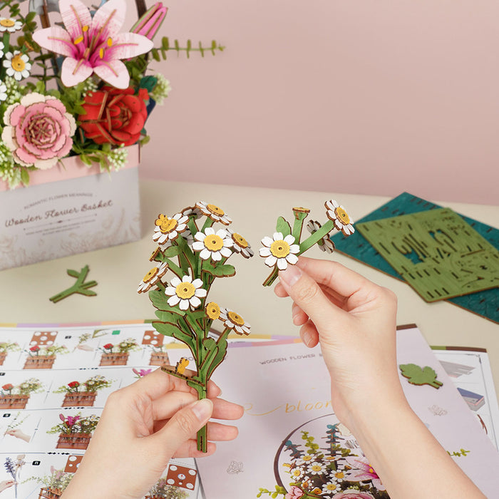 Hands assembling a small white daisy stem from Rowood wooden flower basket puzzle pieces on a craft mat with instruction sheet