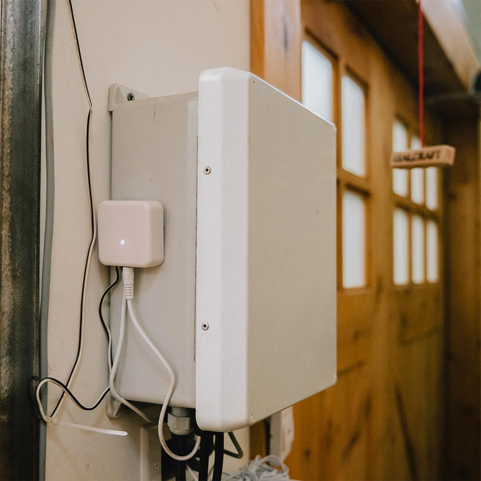 White Franklin Smart Home Connector mounted on a wall with cables connected, blurred wooden carriage door in the background.